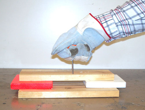 pine board in an elevated position on two supporting blocks, person with leather gloves gripping a block and a nail