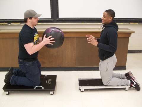 man kneeling on a cart holding a medicine ball, man kneeling on a cart across from him