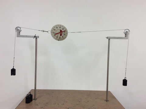 spring scale hangs between two strings which go over pulleys on rods, two masses hung on either side