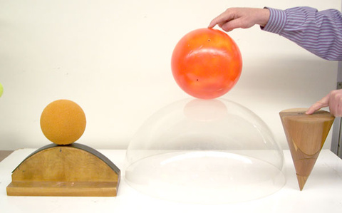 Person holding bowling ball on a Plexiglas Bowl and a inverted cone; ball with offset center of mass on a inverted curved Block with 