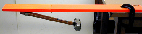 hinged board clamped to a table, hammer underneath board
