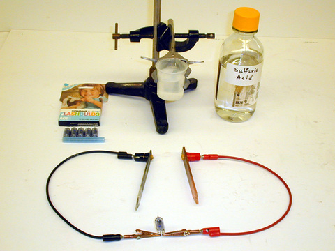 Flash bulbs, magnesium and copper electrodes, beaker, sulfuric acid, tube clamp, and stand